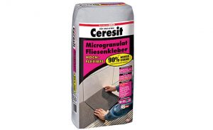 Ein 20-kg-Sack Ceresit Microgranulat Fliesenkleber in grauer Verpackung mit pink-schwarzem Etikett. Der Fliesenkleber ist hochflexibel und wirbt mit 90 % weniger Staubentwicklung. Auf der Vorderseite zeigt ein Foto, wie der Kleber beim Verlegen von Bodenfliesen verwendet wird.
