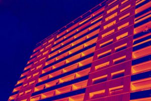 Mehrgeschossiges Gebäude in einer thermografischen Farbpalette, die in Rot-, Gelb- und Blautönen getönt ist. Die verschiedenen Farben heben die Struktur des Gebäudes hervor, während der Hintergrund in einem tiefen Blau gehalten ist.