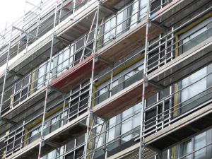 Fassadengerüst mit Arbeitsbühnen an einem mehrstöckigen Gebäude mit großen Fensterflächen während Sanierungsarbeiten.