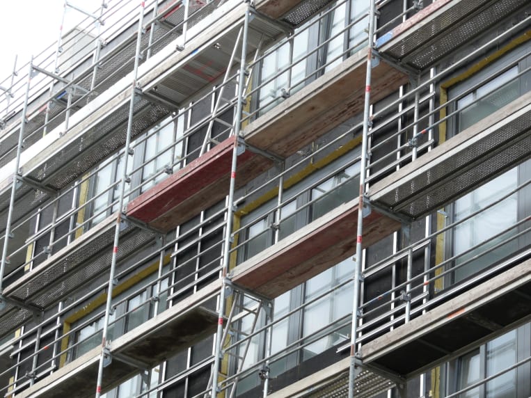 Fassadengerüst mit Arbeitsbühnen an einem mehrstöckigen Gebäude mit großen Fensterflächen während Sanierungsarbeiten.