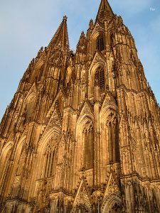 Fassade des Kölner Doms aus Obernkirchener Sandstein in der Abendsonne, mit detailreichen gotischen Verzierungen, Spitzbögen und zwei monumentalen Türmen.