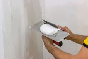 Maler trägt mir einer Spachtel weißen Gipsputz auf eine Wand auf