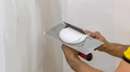Maler trägt mir einer Spachtel weißen Gipsputz auf eine Wand auf