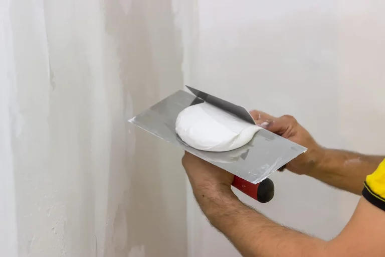 Maler trägt mir einer Spachtel weißen Gipsputz auf eine Wand auf