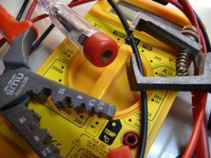 Ein Satz elektrischer Werkzeuge, darunter ein Multimeter, eine Abisolierzange, Messleitungen und ein Spannungsprüfer, auf einem Tisch liegend.