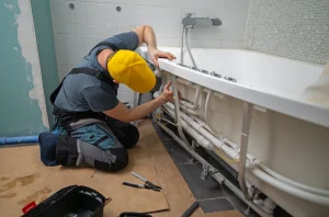 Handwerker installiert die Unterkonstruktion und Rohre einer Badewanne.