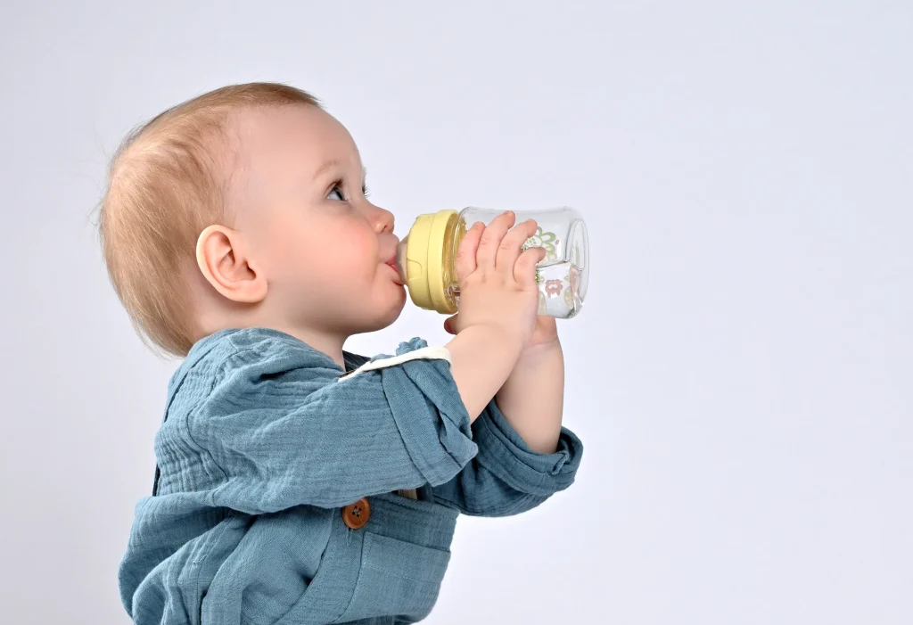 Kleinkind trinkt frisches Trinkwasser aus einer transparenten Babyflasche.