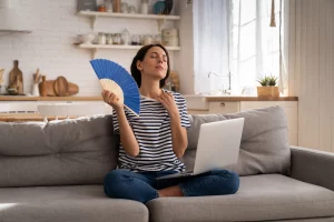 Frau sitzt auf einer Couch und fächert sich Luft mich Fächer zu