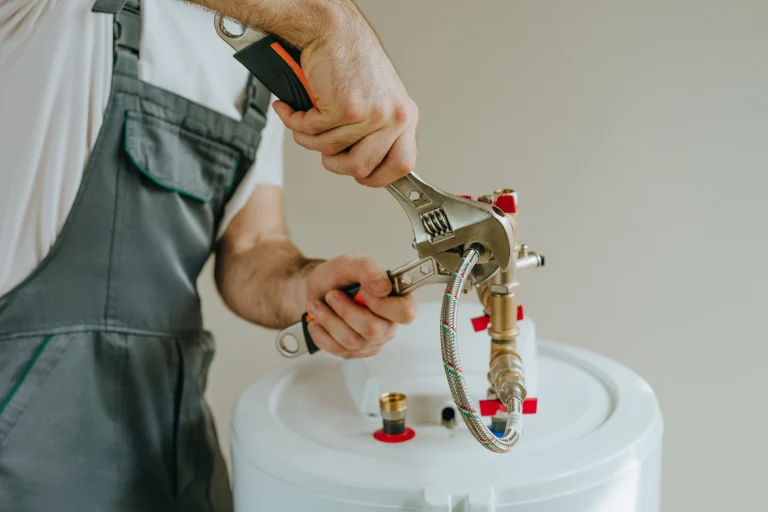 Handwerker schraubt Flexschläuche und Messing-Wasserleitungen an einen Warmwasserspeicher.