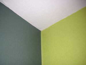 Ecke eines Zimmers mit zwei farbigen Wänden: die linke Wand ist olivgrün und die rechte Wand hellgrün. Die Decke ist weiß. Die verschiedenen Farben verleihen dem Raum einen markanten Kontrast.