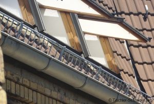 Dach mit Ziegeldeckung und mehreren nach außen geöffneten Dachfenstern mit Holzrahmen und hellen Außenklappen als Sonnen- oder Hitzeschutz.