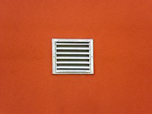 Lüftungsgitter in einer orangefarbenen Außenwand zur Belüftung oder Entlüftung von Innenräumen oder technischen Anlagen.