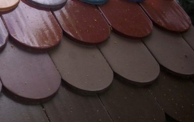 Detailaufnahme farbiger Flachziegel auf einem Dachmodell. Die glasierten Ziegel in verschiedenen Farben wie Rot, Blau, Grün, Violett und Braun sind überlappend verlegt und zeigen eine klassische Rundschnittform am unteren Rand.
