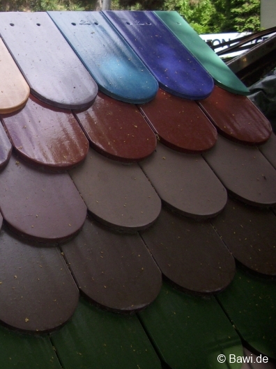 Detailaufnahme farbiger Flachziegel auf einem Dachmodell. Die glasierten Ziegel in verschiedenen Farben wie Rot, Blau, Grün, Violett und Braun sind überlappend verlegt und zeigen eine klassische Rundschnittform am unteren Rand.