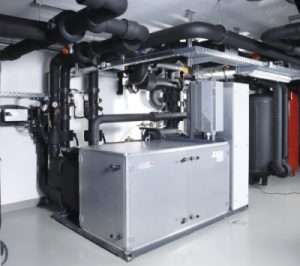Industriekühlsystem in einem technischen Raum. Zu sehen sind zahlreiche Rohre, ein großer grauer Kasten und verschiedene Anschlüsse. Die Umgebung wirkt sauber und ordentlich installiert, mit schwarzer Isolierung auf den Rohren.