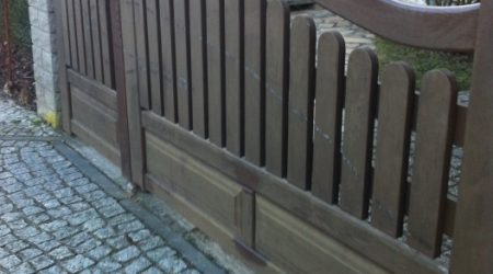 Großes zweiflügeliges Holztor mit geschwungener Oberkante und senkrechten Latten, eingebettet in eine gepflasterte Einfahrt.