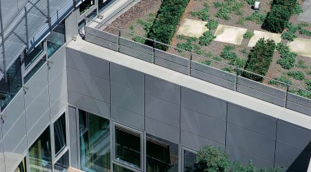 Begrüntes Flachdach eines modernen Bürogebäudes mit klar abgegrenzten Pflanzenflächen und einer umlaufenden Kiesfangleiste am Dachrand zur Sicherung von Substrat und Drainage.