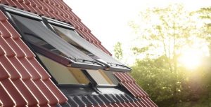 Zwei geöffnete Dachfenster mit außenliegendem Sonnenschutz auf einem roten Ziegeldach bei Sonnenschein.