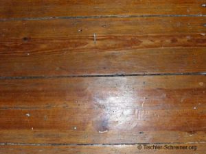 Abgenutzte, alte Holzdielen mit sichtbaren Gebrauchsspuren und natürlicher Holzmaserung in warmem Braunton.