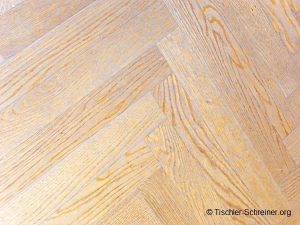 Heller Holzboden mit Fischgrätmuster aus naturbelassenen Eichenholzdielen mit feiner Maserung.