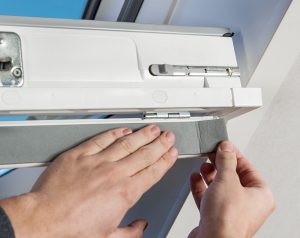 Nahaufnahme von Händen, die eine Dichtungsfolie an einem Dachfenster anbringen.