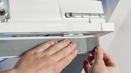 Nahaufnahme von Händen, die eine Dichtungsfolie an einem Dachfenster anbringen.