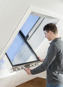 Mann öffnet ein Dachfenster in einem hellen Dachgeschossraum.