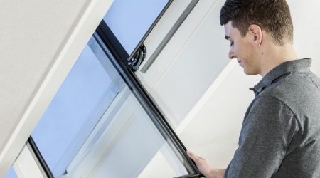 Mann öffnet ein Dachfenster in einem hellen Dachgeschossraum.
