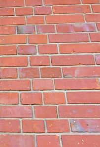 Nahaufnahme einer Wand mit roten Klinkerriemchen in unregelmäßigem Verband. Die schmalen, rechteckigen Ziegel imitieren klassisches Mauerwerk und zeigen leichte Farb- und Oberflächenunterschiede.