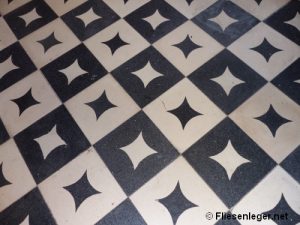 Schwarz-weiß gemusterter Fliesenboden mit rhombenförmigen Designs auf jedem Quadrat. Der Boden zeigt ein geometrisches Muster in einer diagonalen Anordnung.