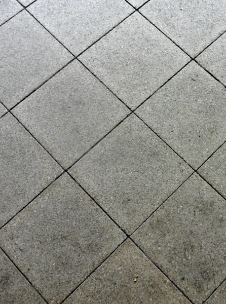 Grau gepflasterter Boden aus quadratischen Platten, diagonal angeordnet. Die Oberfläche wirkt leicht strukturiert und antik. Ein paar kleine Unregelmäßigkeiten in der Farbe verleihen dem Boden einen natürlichen Look. Ideal für städtische oder moderne Designs.
