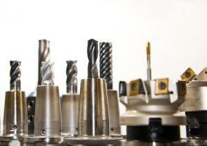 Eine Gruppe von metallischen Bohr- und Fräswerkzeugen steht aufrecht nebeneinander. Die Werkzeuge variieren in Form und Größe, einige haben spiralförmige Schneiden. Der Hintergrund ist weiß, und die Werkzeuge sind scharf im Fokus.