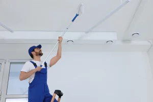 Mann streicht die Decke mit einer Rolle