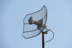 Gitterparabolantenne zur Richtfunk- oder WLAN-Verbindung, montiert auf einem Metallmast vor klarem Himmel.