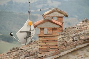 Ziegelgedecktes Dach mit gemauerten Schornsteinen und einer Satellitenschüssel mit Antenne, montiert zur Fernsehempfangsanlage in ländlicher Umgebung.