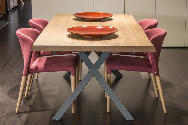 Moderner Esstisch mit massiver Holzplatte und X-förmigem Metallgestell, umgeben von sechs gepolsterten Stühlen in Altrosa; zwei dekorative rote Schalen als Blickfang auf dem Tisch.