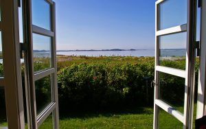 Geöffnete Terrassentüren mit Wärmeschutzverglasung bieten freien Blick auf eine sonnige Küstenlandschaft. Die Isolierverglasung sorgt für optimale Energieeffizienz trotz großer Fensterflächen.