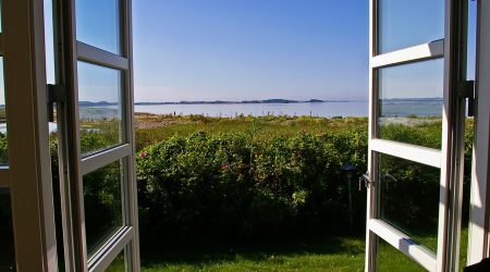 Geöffnete Terrassentüren mit Wärmeschutzverglasung bieten freien Blick auf eine sonnige Küstenlandschaft. Die Isolierverglasung sorgt für optimale Energieeffizienz trotz großer Fensterflächen.