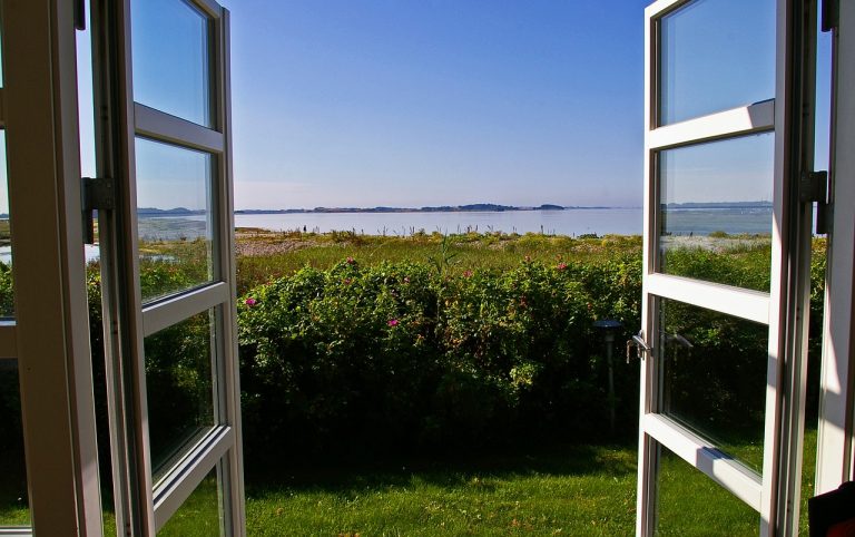 Geöffnete Terrassentüren mit Wärmeschutzverglasung bieten freien Blick auf eine sonnige Küstenlandschaft. Die Isolierverglasung sorgt für optimale Energieeffizienz trotz großer Fensterflächen.