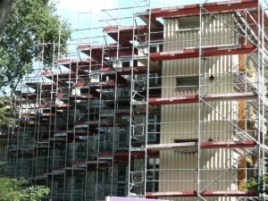 Fassadengerüst mit auskragenden Konsolen an einem mehrgeschossigen Wohngebäude im Grünen zur Sanierung oder Modernisierung.