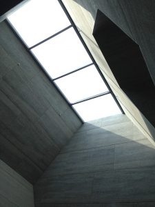 Modernes Glasdach mit großen, rechteckigen Oberlichtern in einem minimalistischen Innenraum mit grauen Wandverkleidungen – sorgt für natürliche Lichtdurchflutung.