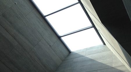 Modernes Glasdach mit großen, rechteckigen Oberlichtern in einem minimalistischen Innenraum mit grauen Wandverkleidungen – sorgt für natürliche Lichtdurchflutung.