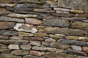 Detailansicht einer naturbelassenen Trockenmauer aus unregelmäßig geschichteten Natursteinen im Gartenbau.