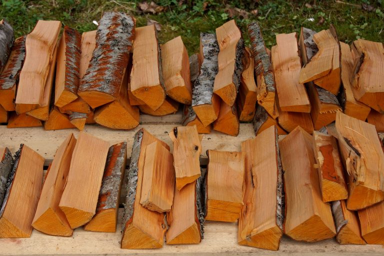 Gestapeltes, gespaltenes Brennholz mit Rinde auf einer Holzpalette im Freien.