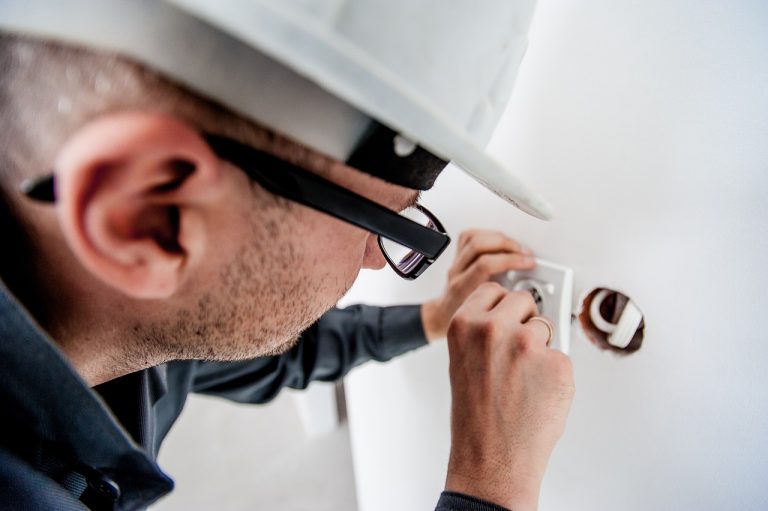 Elektriker mit Schutzhelm bei der Unterputz-Montage eines Bewegungsmelders in einer Wanddose
