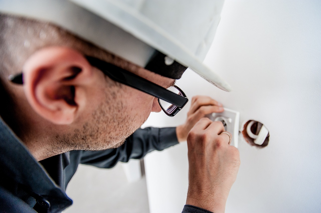 Elektriker mit Schutzhelm bei der Unterputz-Montage eines Bewegungsmelders in einer Wanddose