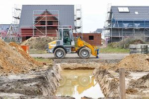 Baustelle mit Bagger, Baugrube und Neubauten im Rohbau – Symbol für Hausbau, Erdarbeiten und Immobilienentwicklung in einem Neubaugebiet.