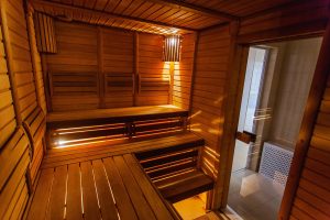 Eine gemütliche Holzsauna mit mehreren Sitzbänken und sanfter Beleuchtung. Ein kleines Fenster bietet einen Blick nach draußen. Die warme, einladende Atmosphäre lädt zum Entspannen ein.