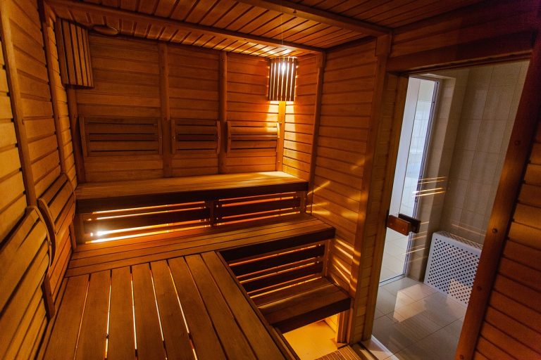 Eine gemütliche Holzsauna mit mehreren Sitzbänken und sanfter Beleuchtung. Ein kleines Fenster bietet einen Blick nach draußen. Die warme, einladende Atmosphäre lädt zum Entspannen ein.