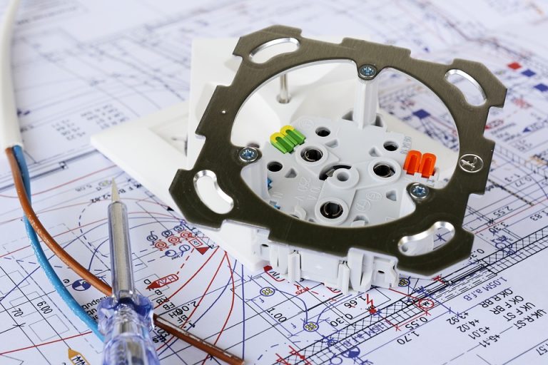 „Nahaufnahme einer Unterputzsteckdose auf einem technischen Stromplan, mit abisolierten Kabeln und Spannungsprüfer – Vorbereitung zum Anschluss eines Herdes.